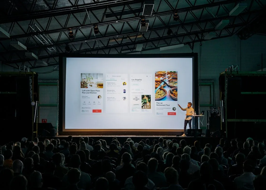 A speaker presenting to an audience in a darkened room