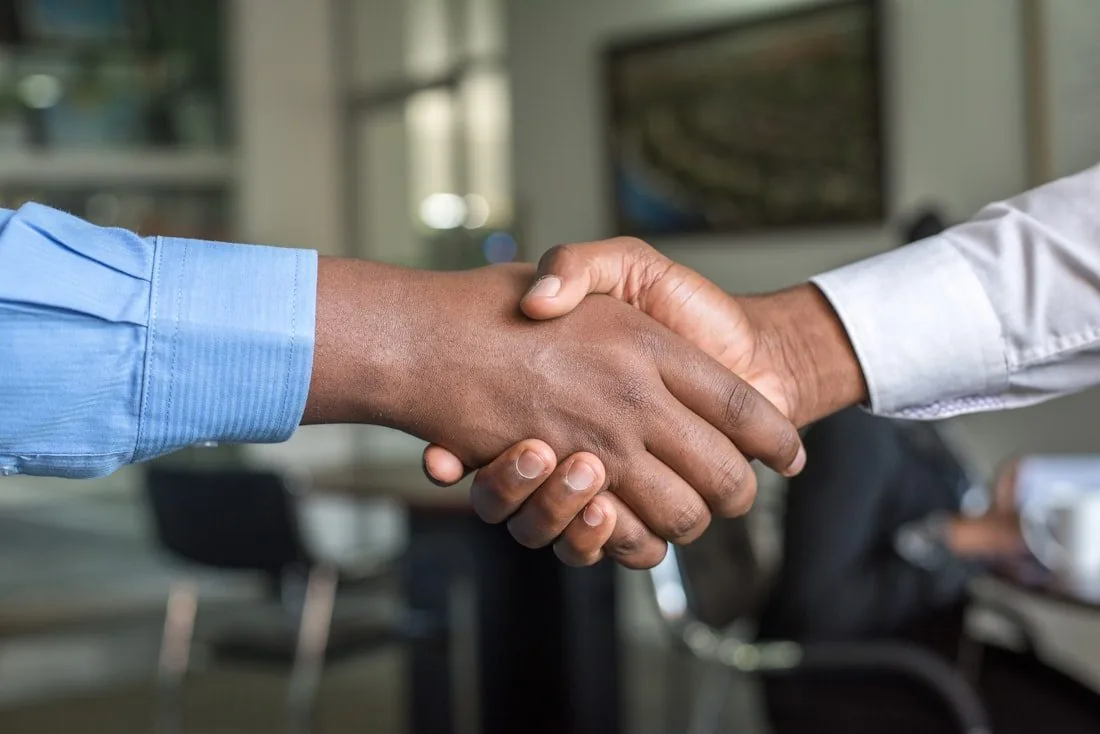 Two people in shirtsleeves shaking hands in an office, standing for delegated authority