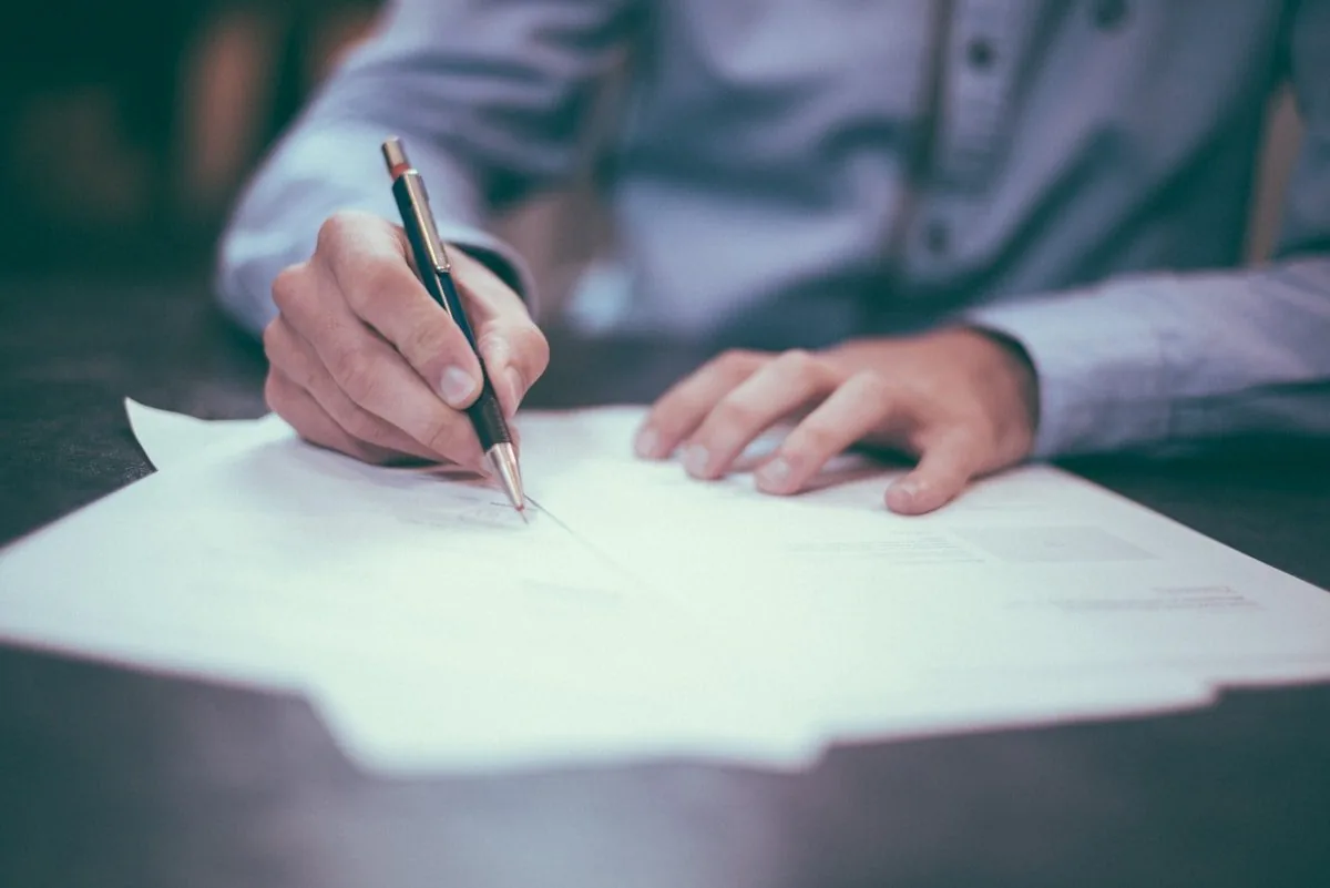 A hand signing a document, standing for supervision and sign-off